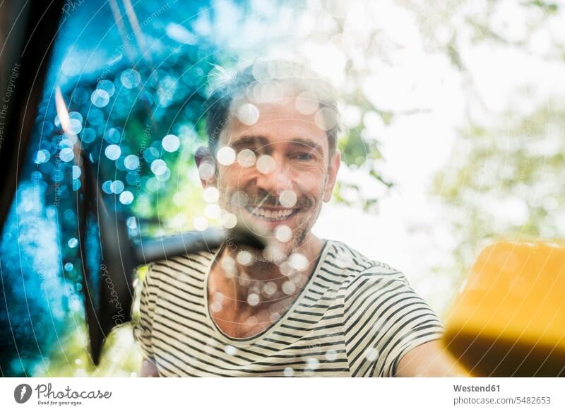 Portrait of smiling mature man washing windscreen of his car automobile Auto cars motorcars Automobiles men males motor vehicle road vehicle road vehicles