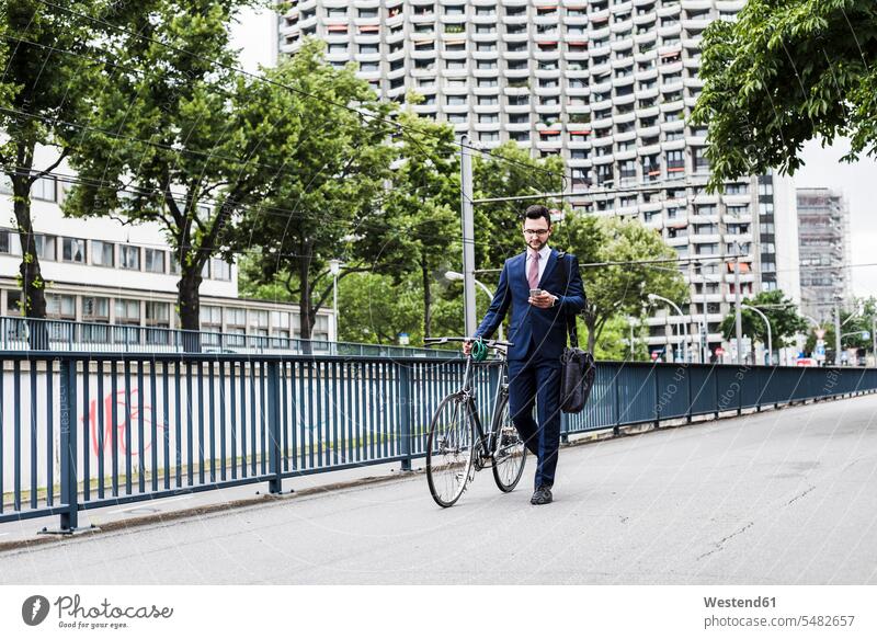Businessman with bicycle walking in the city, using smart phone bikes bicycles pushing going text messaging SMS Text Message mobile phone mobiles mobile phones