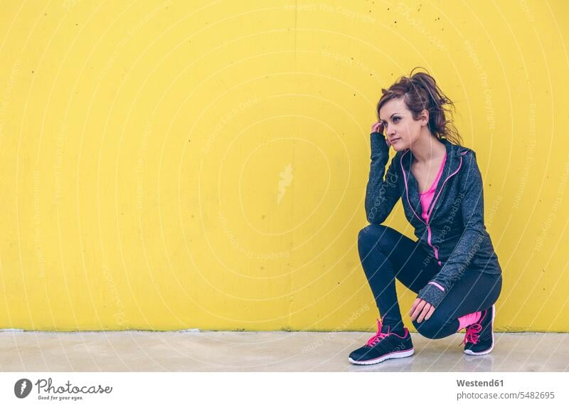 Woman wearing sports wear crouching in front of yellow wall caucasian caucasian ethnicity caucasian appearance european Activity active Contemplation reflection