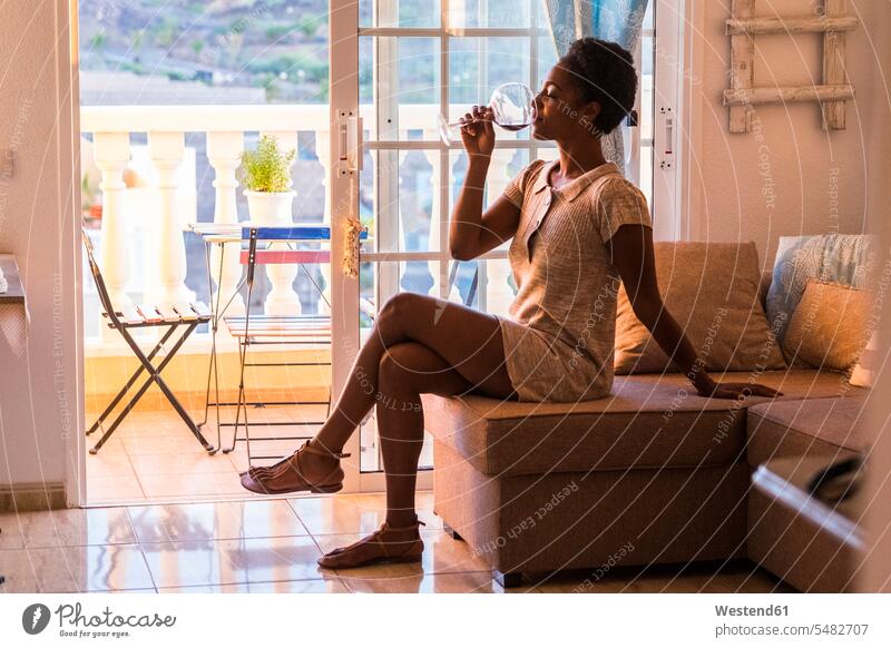 Young woman sitting on the couch drinking glass of red wine females women Seated Adults grown-ups grownups adult people persons human being humans human beings