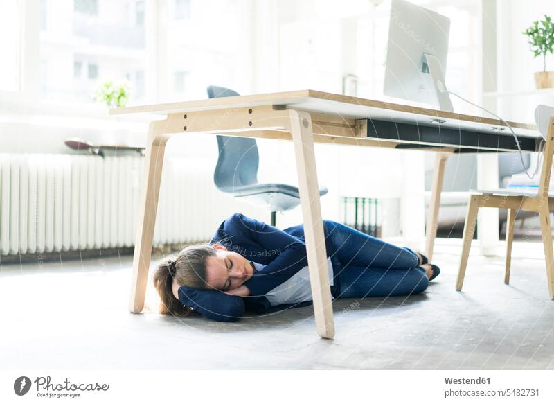 Businesswoman lying under the table in office sleeping laying down lie lying down businesswoman businesswomen business woman business women asleep females