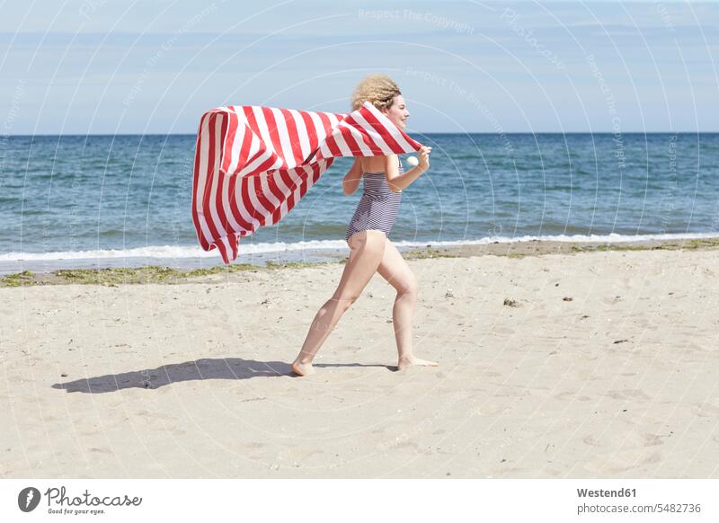 Smiling young woman with beach towel in front of the sea females women Beach Towel beaches Adults grown-ups grownups adult people persons human being humans