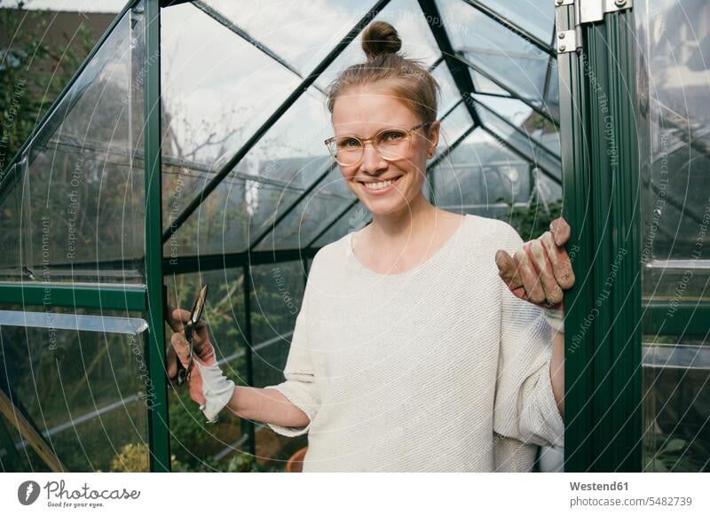 Portrait of smiling young woman standing in the door of her greenhouse females women portrait portraits hot house glass house glass houses hot houses Adults