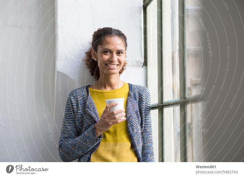 Young woman standing at the window with a cup of coffee Coffee Coffee Cup Coffee Cups drinking windows females women Drink beverages Drinks Beverage