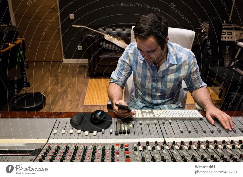 Man in the control room of a recording studio looking at cell phone Mixing Console mixer mixing board Recording Studio audio engineer audio technician