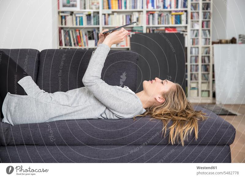 Young woman lying on couch using digital tablet beautiful Joy enjoyment pleasure Pleasant delight smiling smile casual leisure wear casual clothing casual wear