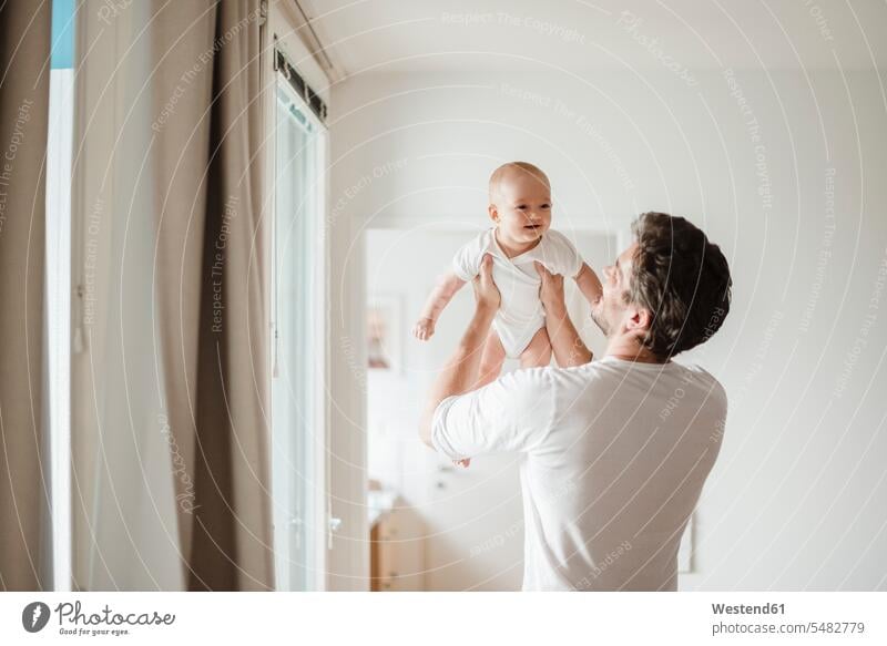 Father holding baby girl at home father pa fathers daddy dads papa infants nurselings babies smiling smile parents family families people persons human being