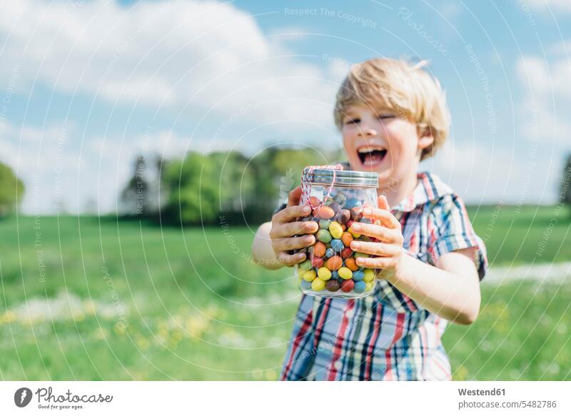 Happy boy outdoors holding glass with jelly beans boys males jellybean Fun having fun funny child children kid kids people persons human being humans