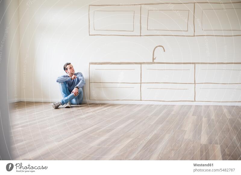 Young man in new home sitting on floor thinking about interior design flat flats apartment apartments Seated males Adults grown-ups grownups adult people