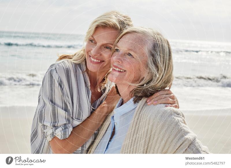 Senior woman and her adult daughter standing on the beach, embracing beaches mother mommy mothers mummy mama daughters together embrace Embracement hug hugging