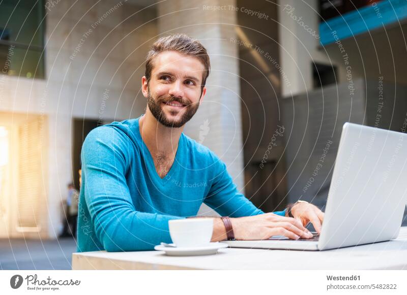 Smiling young man sitting at table using laptop Laptop Computers laptops notebook men males smiling smile computer computers Adults grown-ups grownups adult
