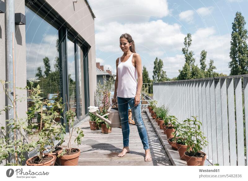 Smiling woman on balcony holding watering can females women relaxed relaxation smiling smile balconies watering cans Adults grown-ups grownups adult people
