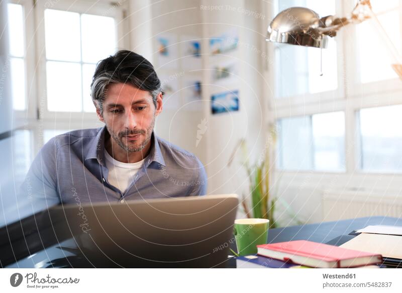 Man using laptop at desk in office Laptop Computers laptops notebook offices office room office rooms Businessman Business man Businessmen Business men males