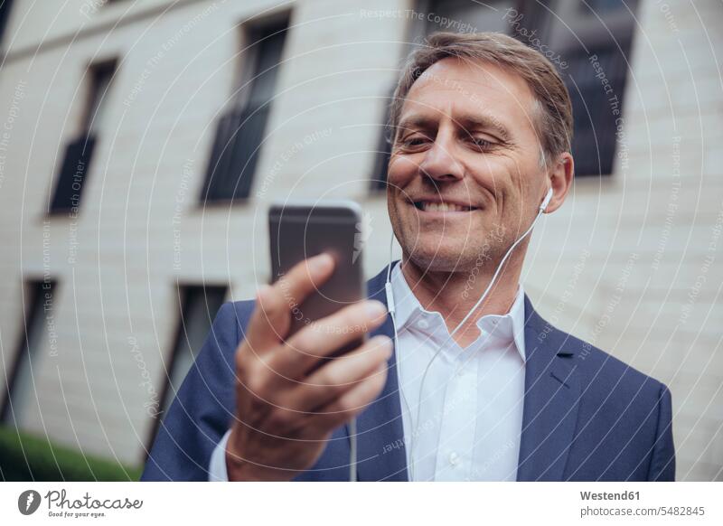 Portrait of smiling mature businessman outdoors with earphones and smartphone mobile phone mobiles mobile phones Cellphone cell phone cell phones Businessman