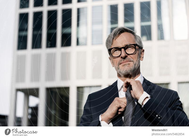 Grey-haired businessman adjusting his tie in front of skyscraper Businessman Business man Businessmen Business men neckties Neck Tie portrait portraits