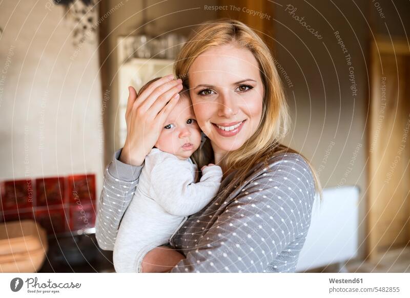 Portrait of smiling mother holding baby at home infants nurselings babies smile mommy mothers ma mummy mama people persons human being humans human beings