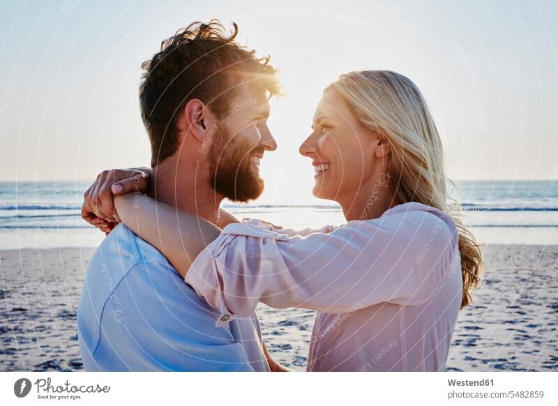 Smiling couple hugging on the beach at sunset smiling smile embracing embrace Embracement happiness happy beaches twosomes partnership couples people persons