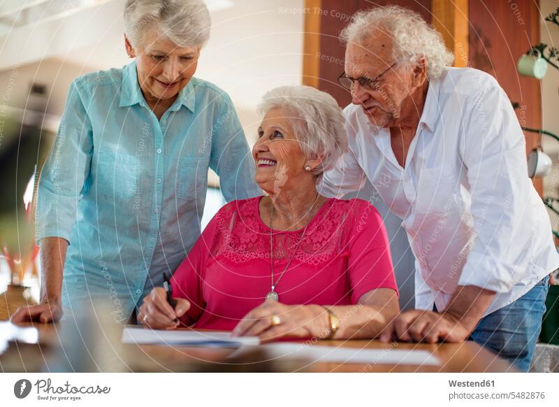 Senior woman signing a contract, friends reassuring her form forms senior women elder women elder woman old senior woman friendship filling in fill in