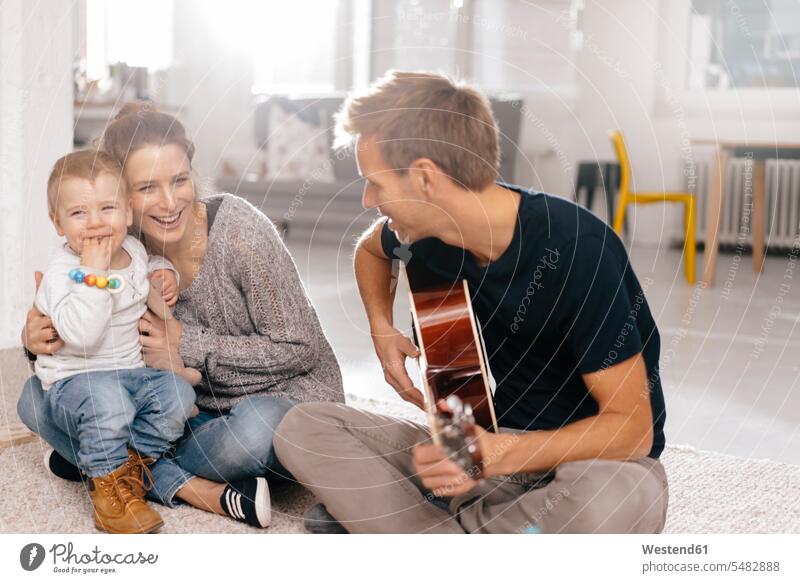 Happy family sitting on the floor with father playing guitar floors pa fathers daddy dads papa families Seated happiness happy guitars parents people persons