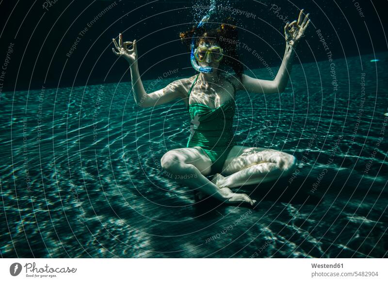 Woman with diving goggles and snorkel sitting in yoga pose underwater in a swimming pool woman females women pools swimming pools submerged Under Water