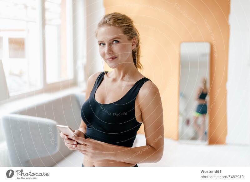 Portrait of smiling young woman in sportswear holding cell phone females women confidence confident mobile phone mobiles mobile phones Cellphone cell phones