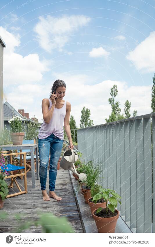 Woman on cell phone on balcony watering plants relaxed relaxation on the phone call telephoning On The Telephone calling balconies smiling smile mobile phone