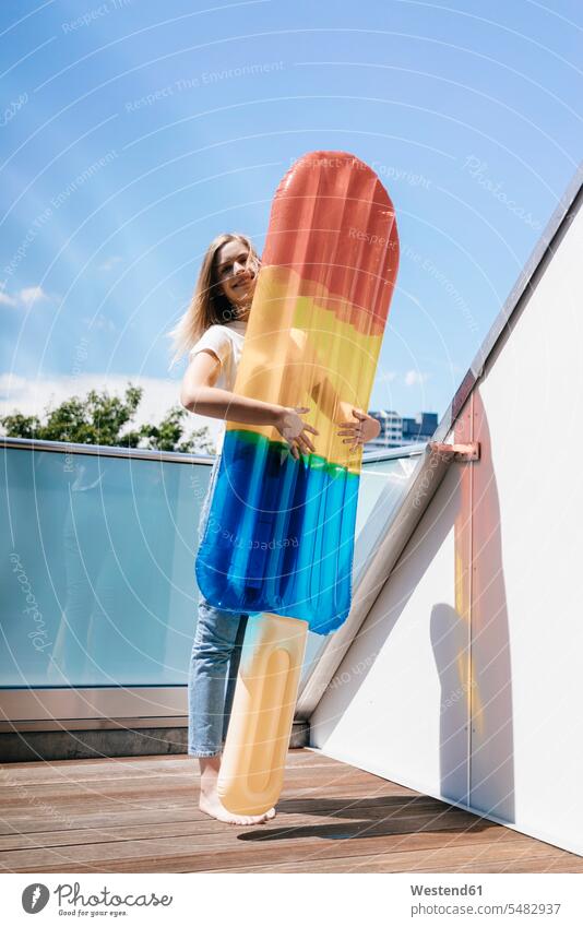 Young woman standing barefoot on balcony with an ice lolly shaped airbed lilos airbeds air beds inflatable mattress air mattress air mattresses naked feet