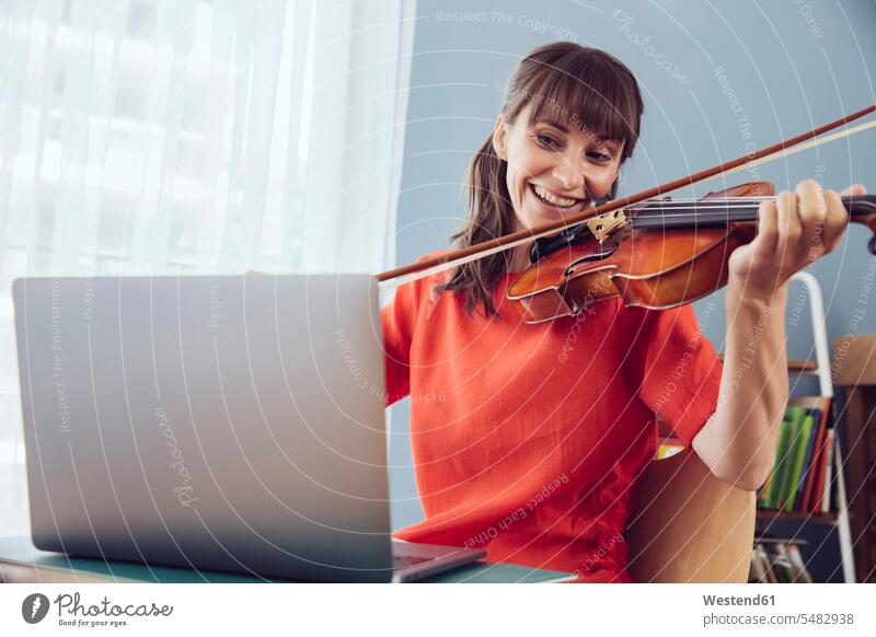 Woman using laptop to play a song on a violin violins practicing practice practise exercise exercising practising Laptop Computers laptops notebook smiling