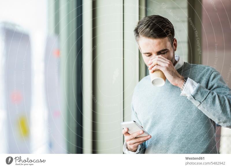 Young man with coffee to go looking at cell phone caucasian caucasian ethnicity caucasian appearance european message information Germany looking down indoors