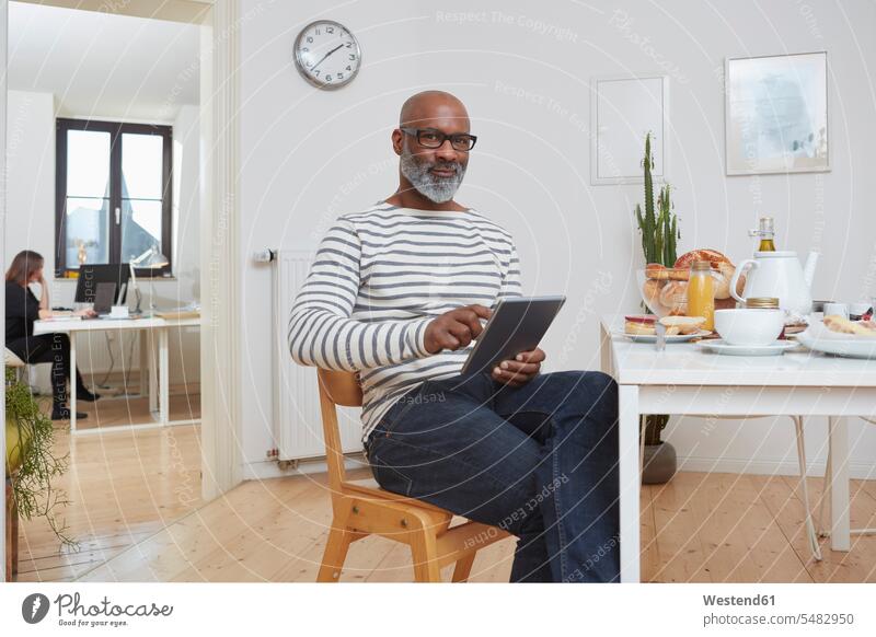 Portrait of smiling man sitting at breakfast table with digital tablet African-American Ethnicity Afro-American African American Ethnicity African Americans
