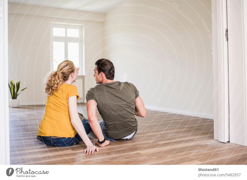 Young couple in new home sitting on floor discussing flat flats apartment apartments Seated talking speaking twosomes partnership couples people persons