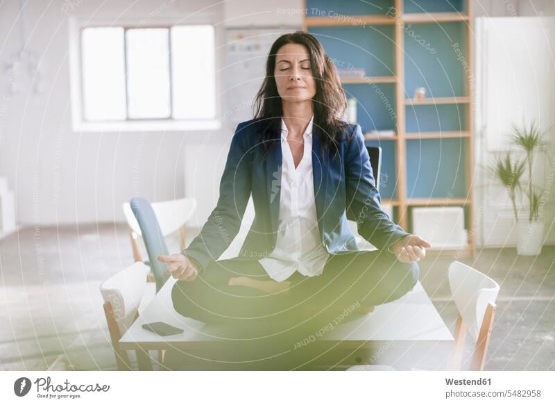 Businesswoman doing yoga exercise on desk in a loft females women Adults grown-ups grownups adult people persons human being humans human beings desks