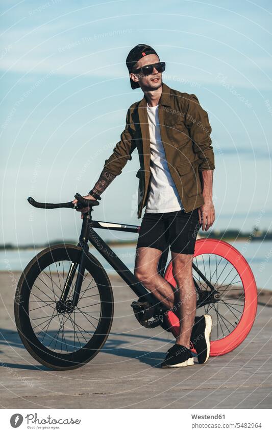 Young man with fixie bike at the waterfront men males River Rivers standing bicycle bikes bicycles Adults grown-ups grownups adult people persons human being