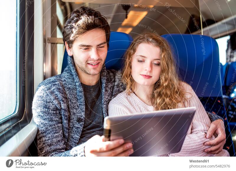 Smiling young couple in train car using digital tablet Travel sitting Seated rail journey train travel train journey young couples young twosome young twosomes