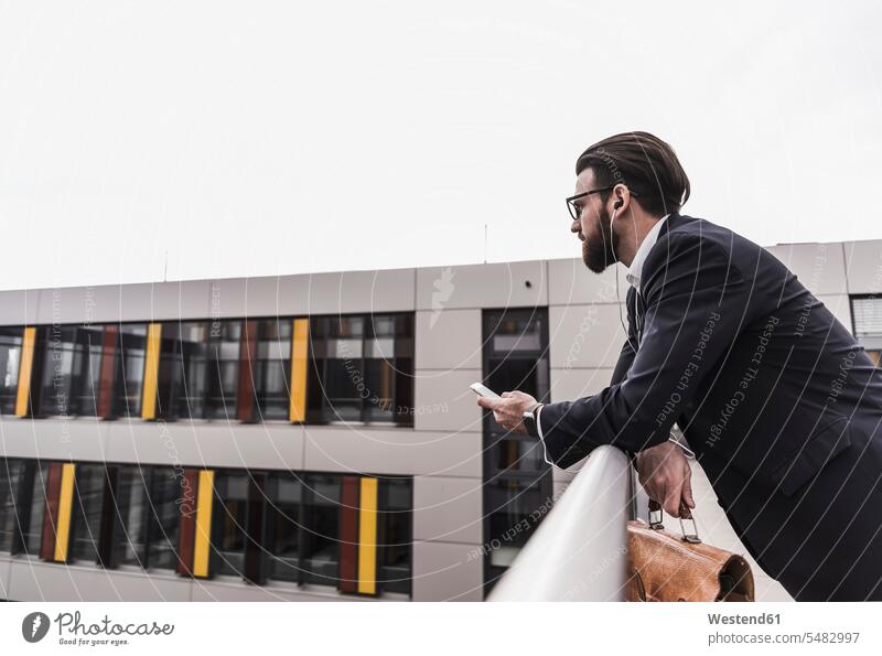 Businessman standing in office building, using smart phone Railing Railings parapet balustrade on the move on the way on the go on the road mobile phone mobiles