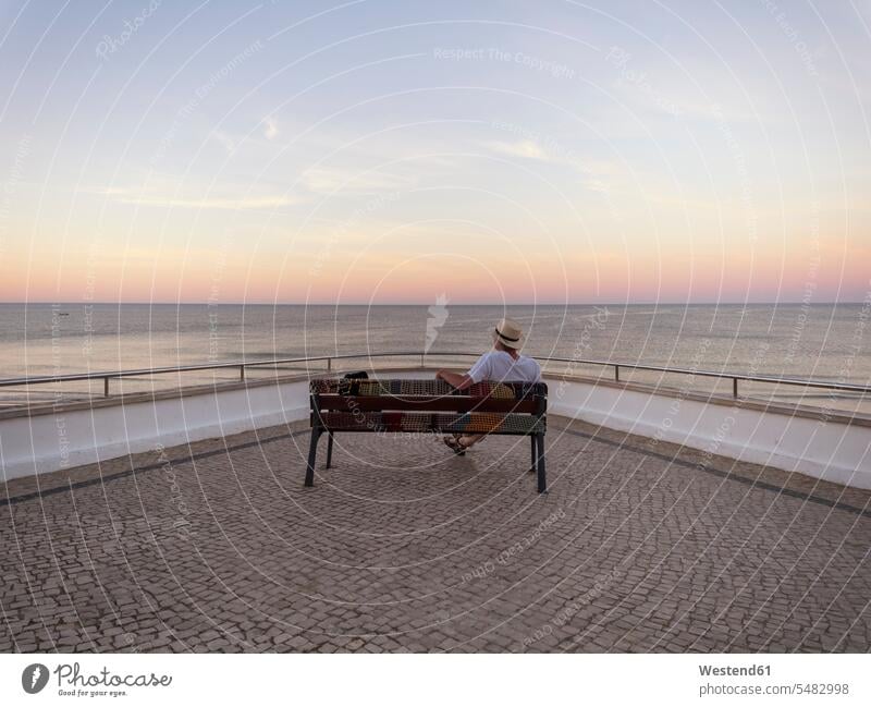 Portugal, Senior man siting on bench watching sunrise men males beach beaches tourist tourists benches sun rise sunrises sitting Seated senior men senior man