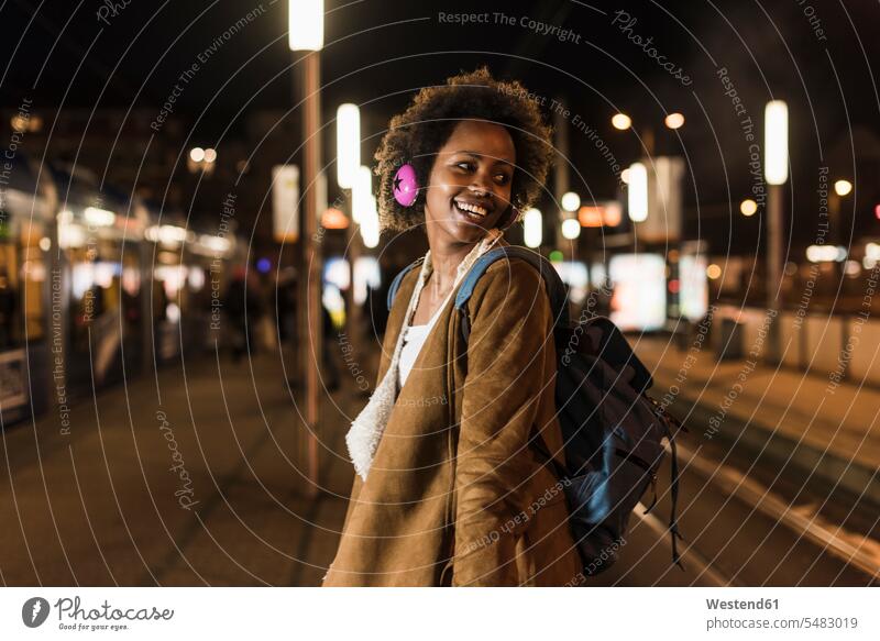 Smiling young woman with headphones and backpack waiting at the tram stop portrait portraits females women Adults grown-ups grownups adult people persons