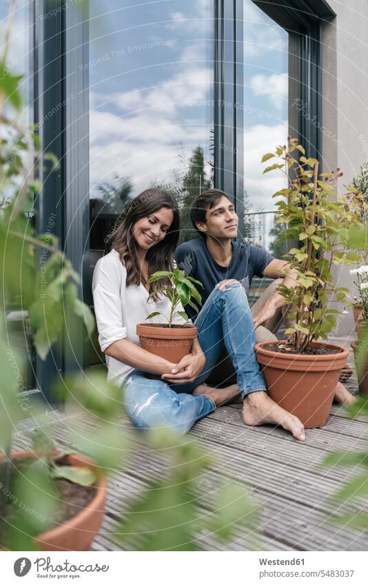 Happy couple with plants relaxing on balcony balconies relaxed relaxation smiling smile twosomes partnership couples sitting Seated people persons human being