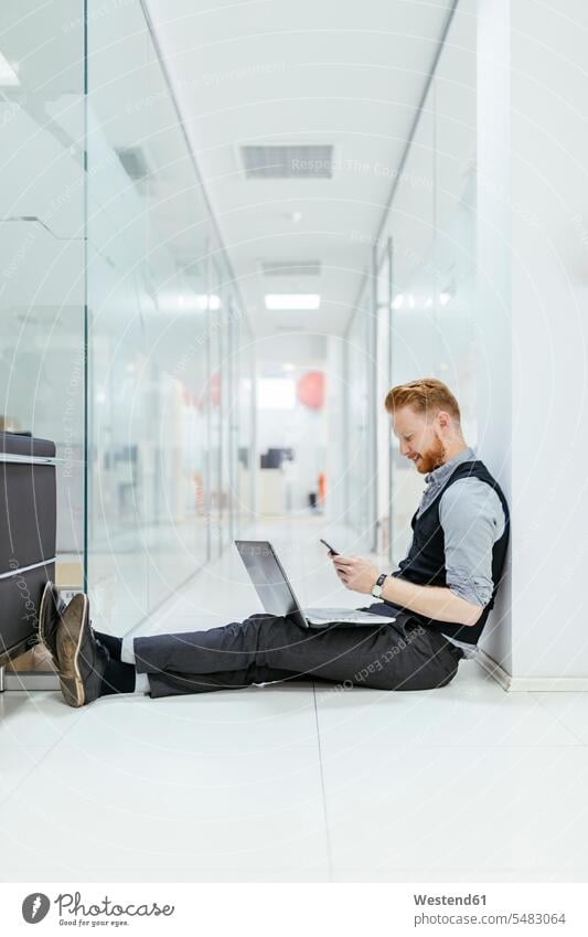 Businessman in office sitting on floor, using laptop Smartphone iPhone Smartphones floors text messaging SMS Text Message Seated reading Laptop Computers