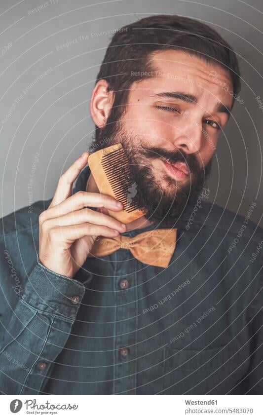 Man combing his beard with a wooden comb, wearing denim shirt and cork bow tie combs man men males portrait portraits Adults grown-ups grownups adult people