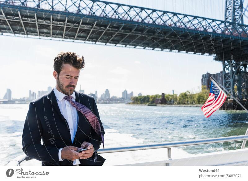 USA, New York City, businessman on ferry on East River checking cell phone New York State Businessman Business man Businessmen Business men mobile phone mobiles