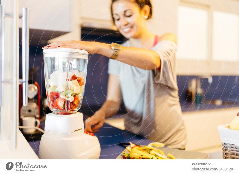 Young woman in kitchen preparing a healthy drink in blender smiling smile smoothie Smoothies females women Drink beverages Drinks Beverage food and drink