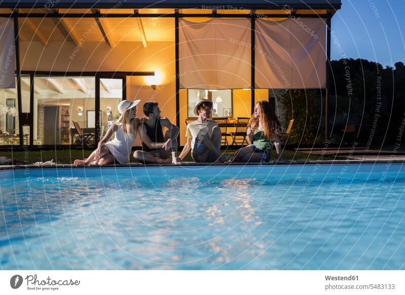 Four friends relaxing at the poolside at evening twilight sitting Seated swimming pool swimming pools friendship pool edge Pool Side in the evening summer