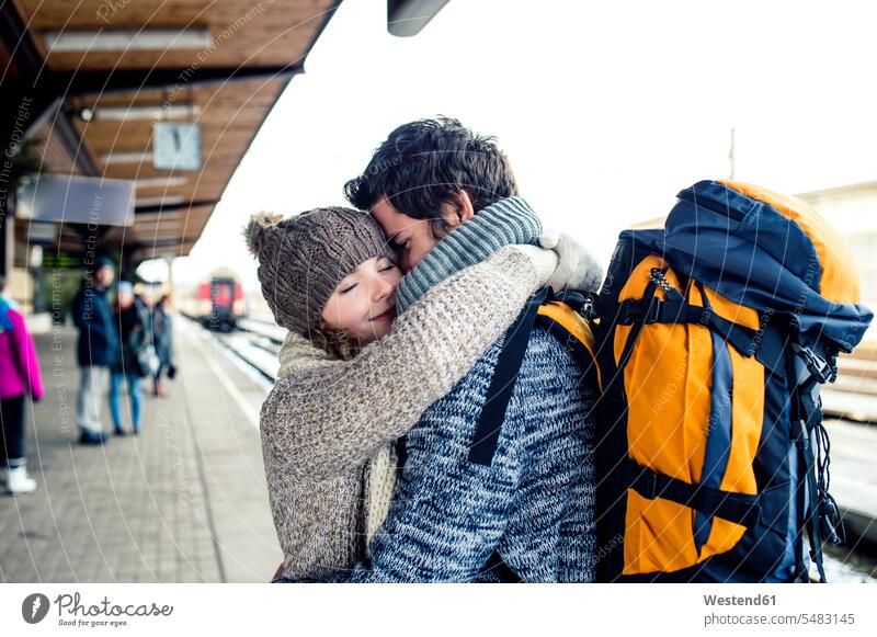 Smiling young couple embracing on station platform train station smiling smile casual leisure wear casual clothing casual wear casual clothes Casual Attire