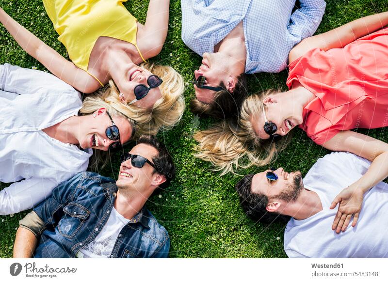 Happy friends wearing sunglasses lying in meadow together Enjoyment Amusement pleasure enjoy enjoying smiling smile bonding community casual leisure wear