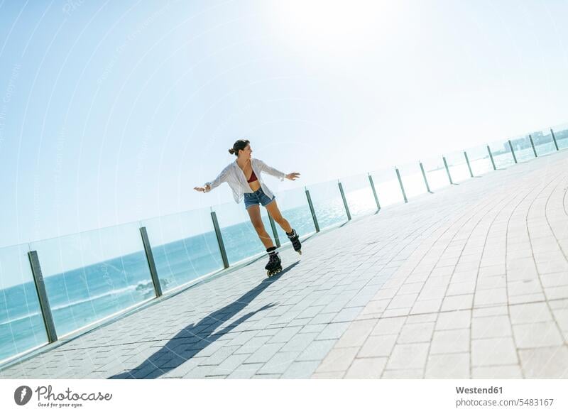 Young woman inline skating on boardwalk at the coast riding inline skates inliners females women Rollerblades rollerskating roller skating rollerblading sport