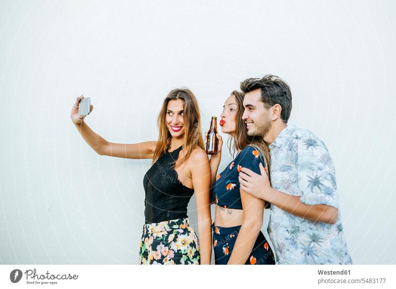 Friends taking a selfie with smartphone in front of white wall friends Fun having fun funny mobile phone mobiles mobile phones Cellphone cell phone cell phones