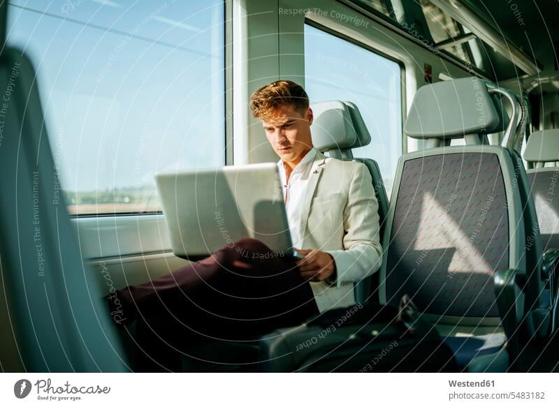 Young man using a laptop on a train Laptop Computers laptops notebook travelling traveling Businessman Business man Businessmen Business men males computer