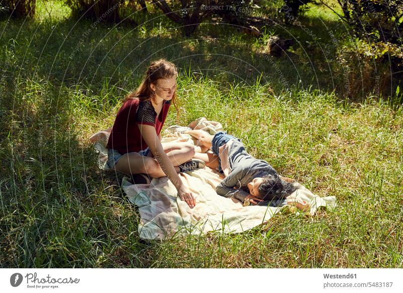 Two friends relaxing on blanket on a meadow meadows woman females women sitting Seated nature natural world Adults grown-ups grownups adult people persons