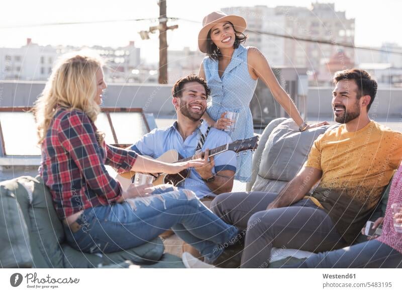Friends having a rooftop party and playing guitar roof terrace deck Fun having fun funny celebrating celebrate partying friends couch settee sofa sofas couches